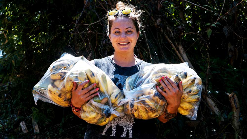 A woman holds two transparent bags with bananas.
